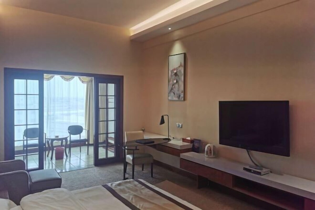 Hotelkamer met een bed, bureau, stoel, televisie en een groot raam met gordijnen.