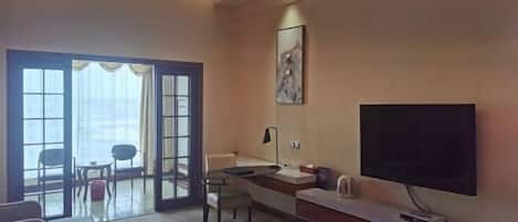 A hotel room with a bed, a desk, a chair, a TV, and a large window with curtains.