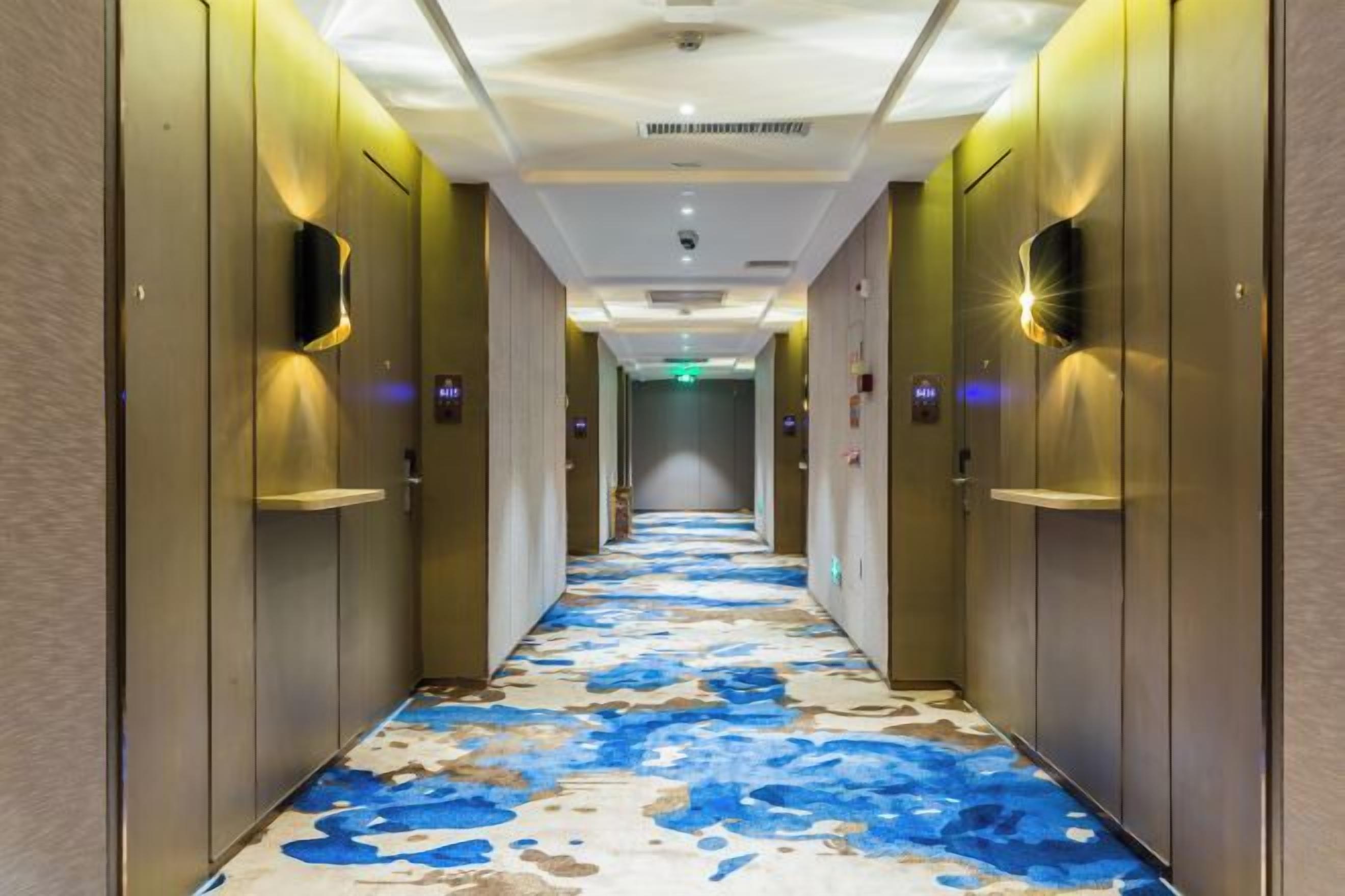 Ein Hotelgang mit einem gemusterten Boden, Türen und Wandleuchten.
