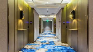 Corredor de hotel com piso estampado, portas e iluminação na parede.