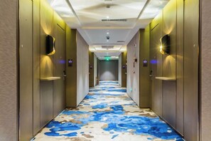 A hotel hallway with a patterned floor, doors, and wall-mounted lighting.