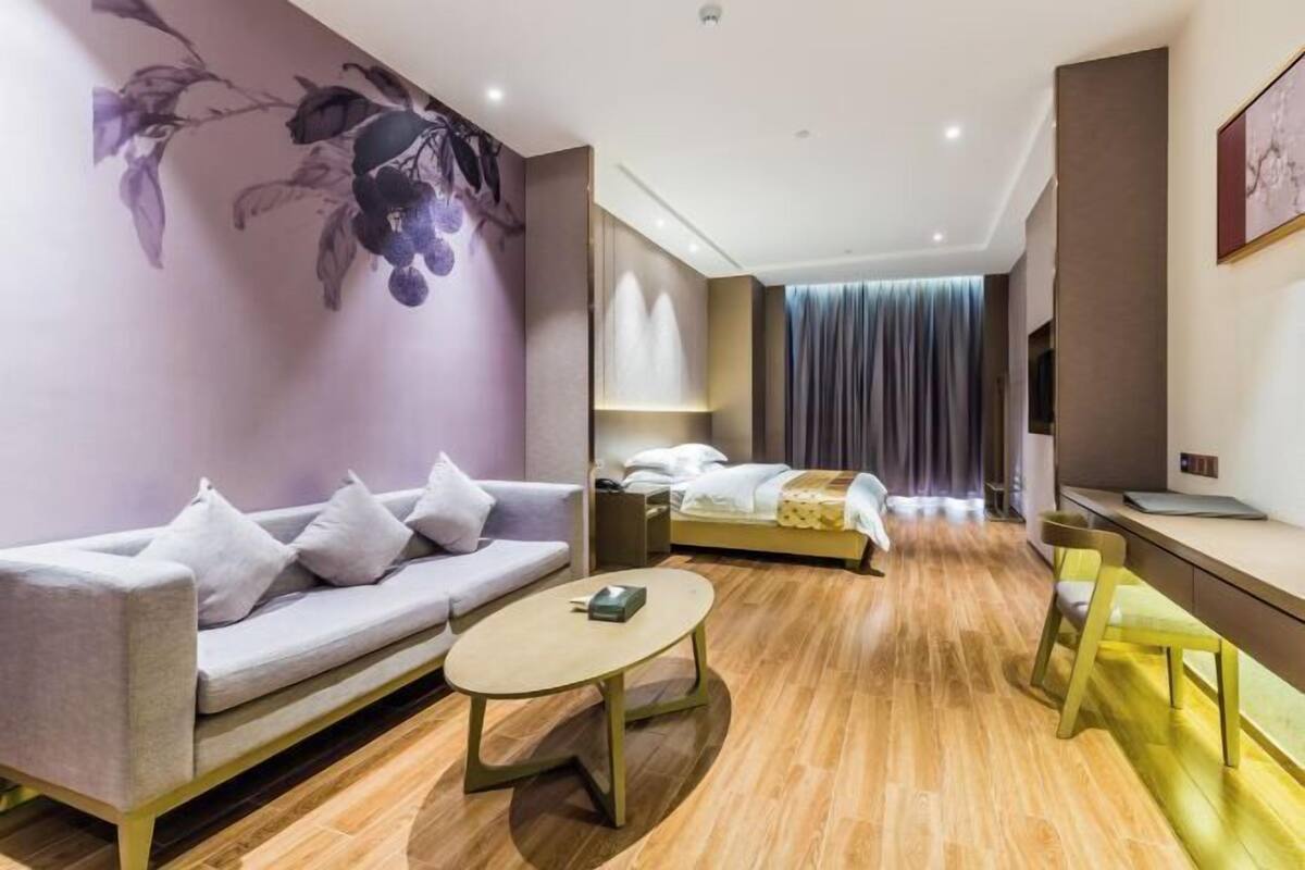 A modern hotel room with a sofa, a bed, a desk, and a mirror.
