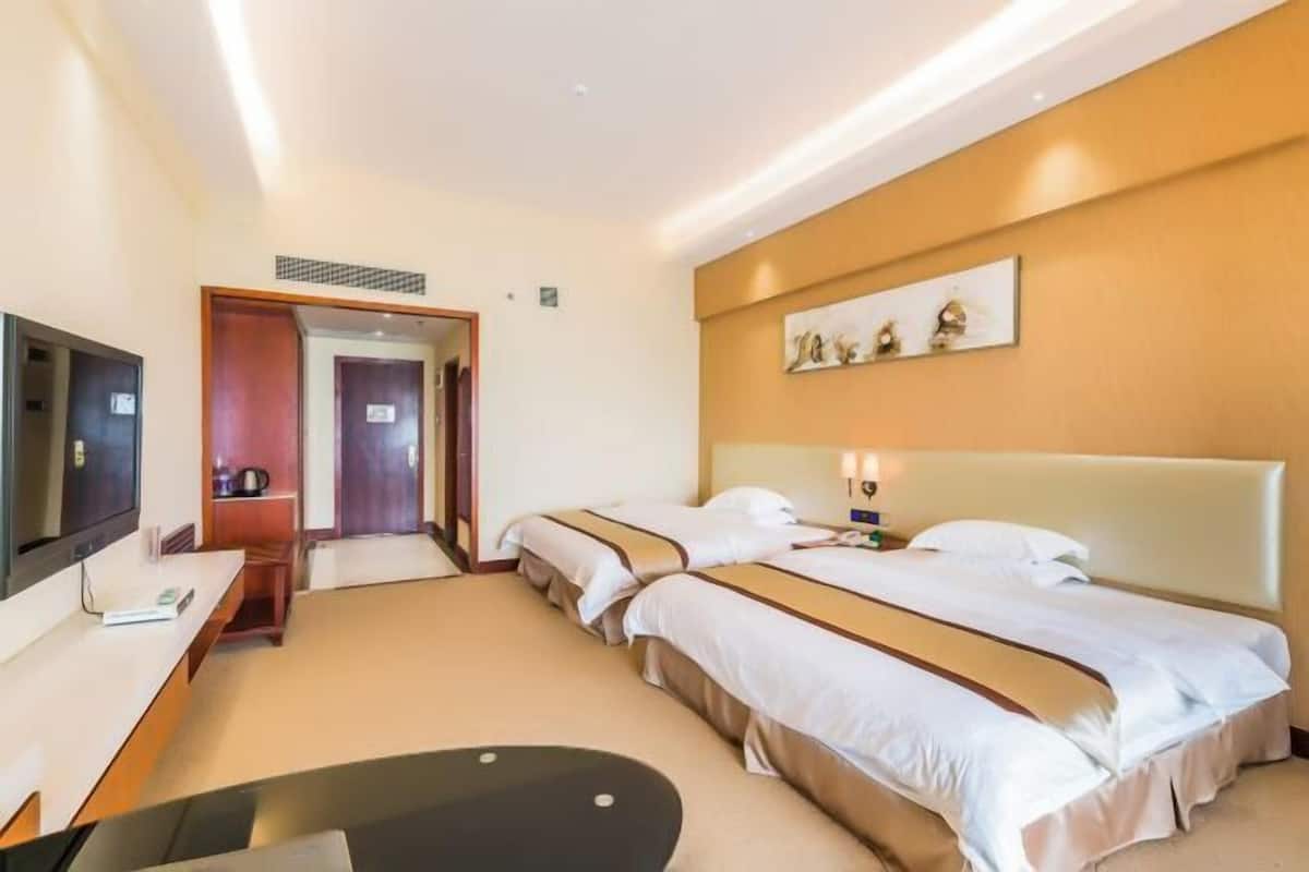 A hotel room with two beds, a desk, a TV, and a door leading to another room.