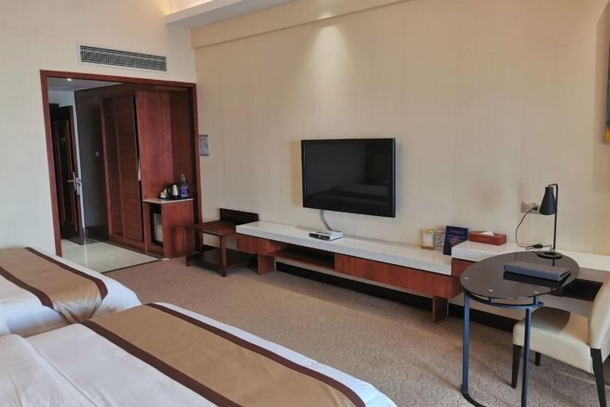 Een hotelkamer met een televisie, een bureau, een stoel en twee bedden.