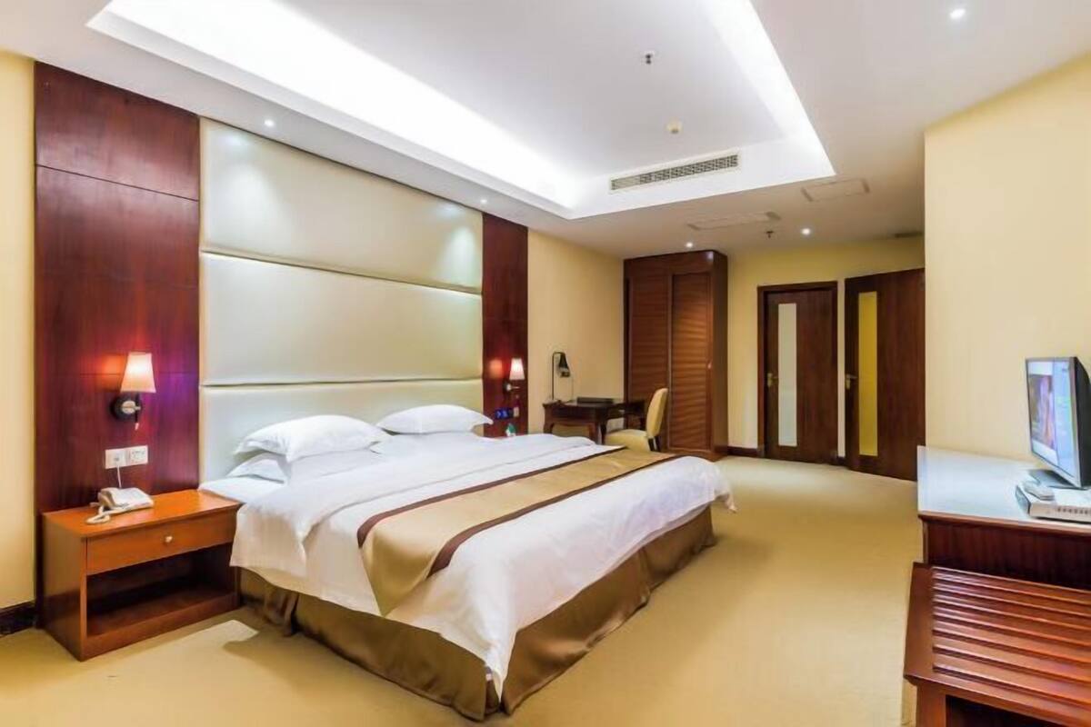A hotel room with a large bed, a desk, a chair, and a television.