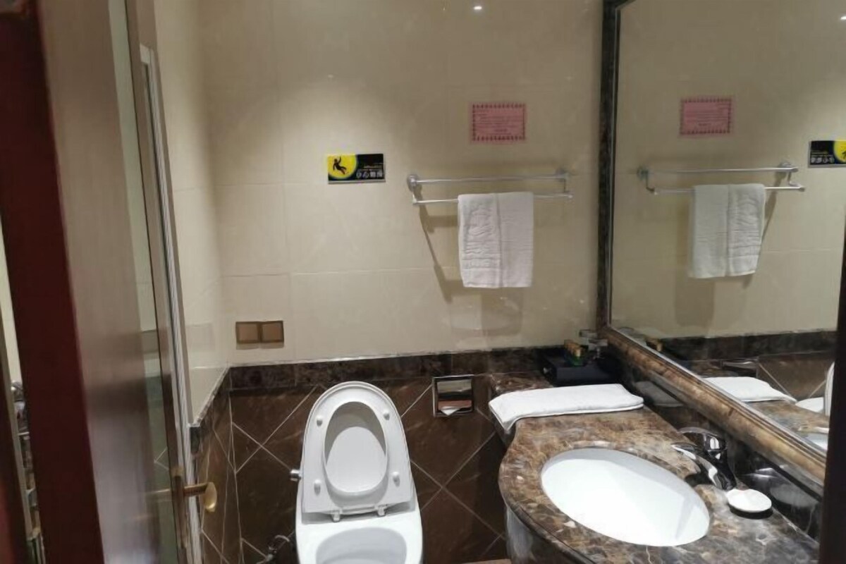 Een badkamer met toilet, wastafel en spiegel. Handdoeken hangen aan de handdoekhouder en er is een bordje aan de muur.