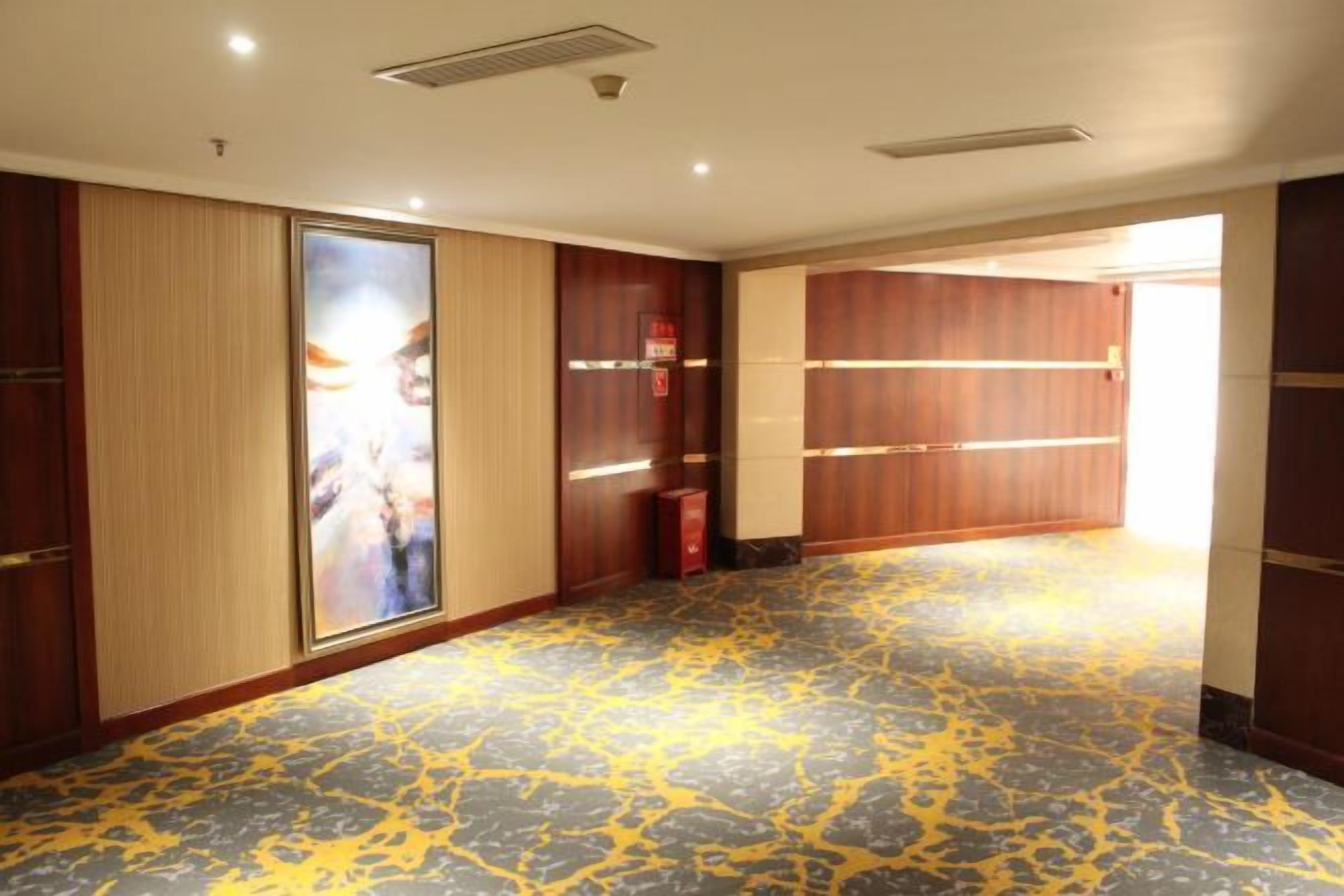 Un pasillo de hotel con puertas de madera, alfombra estampada y un detector de incendios.