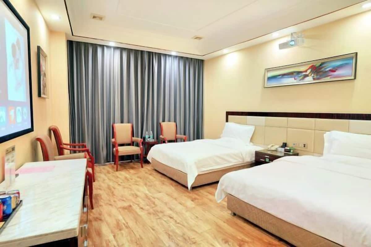 Habitación de hotel con dos camas, un escritorio con silla, una pantalla de televisión y un ventanal con cortinas.