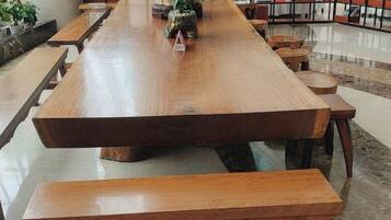 A long wooden table with benches, surrounded by bookshelves and potted plants in a well-lit indoor space.
