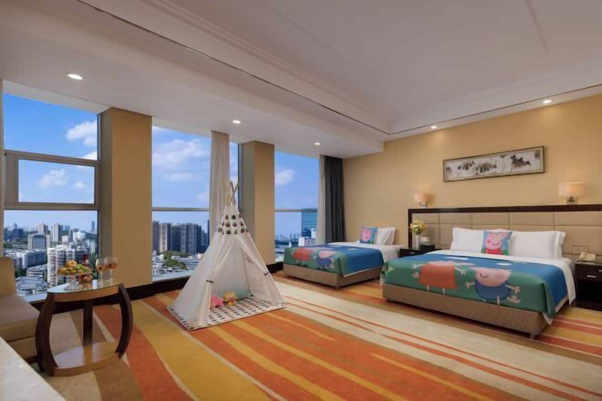 Habitación de hotel con dos camas, vistas a la ciudad, una mesita con fruta y bebidas, y una estructura similar a una tienda de campaña.