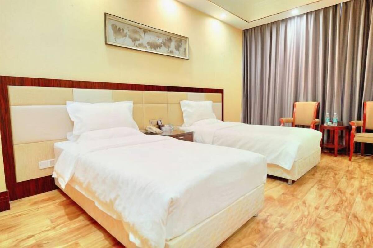 Habitación de hotel con dos camas, piso de madera, un cuadro en la pared y una cortina en la ventana.