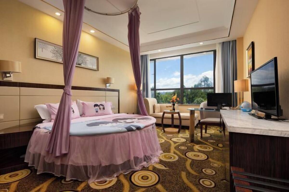 Habitación de hotel con cama, televisión, escritorio y vistas al exterior.