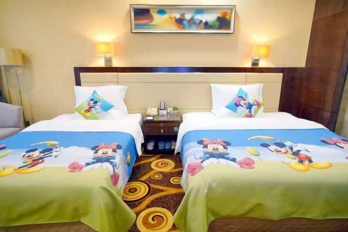 Habitación de hotel con dos camas, cada una con ropa de cama temática de Mickey Mouse. Hay un cuadro en la pared sobre las camas y piso alfombrado.