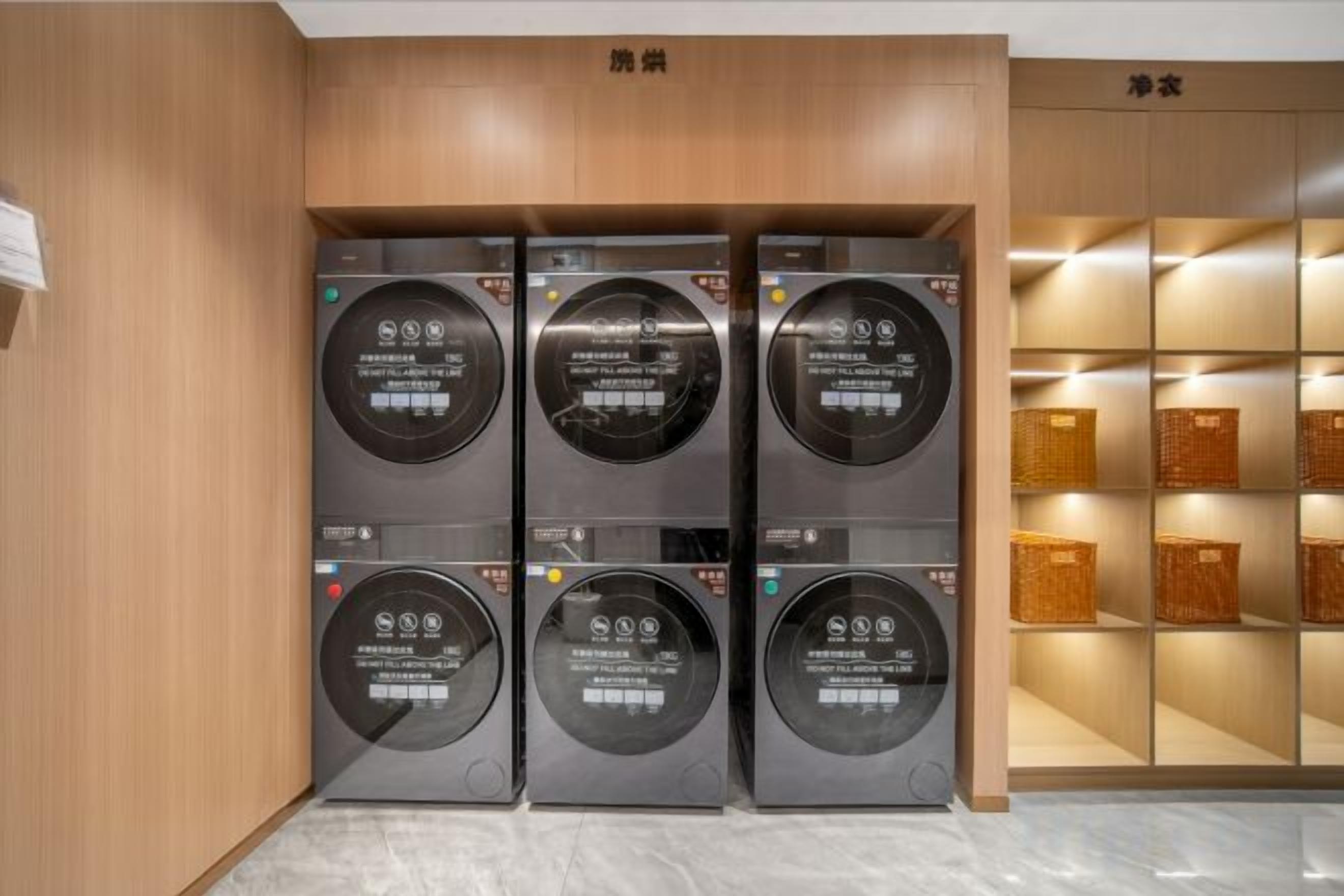 A laundry facility with four washing machines, wooden cabinets above, and baskets on shelves to the right.