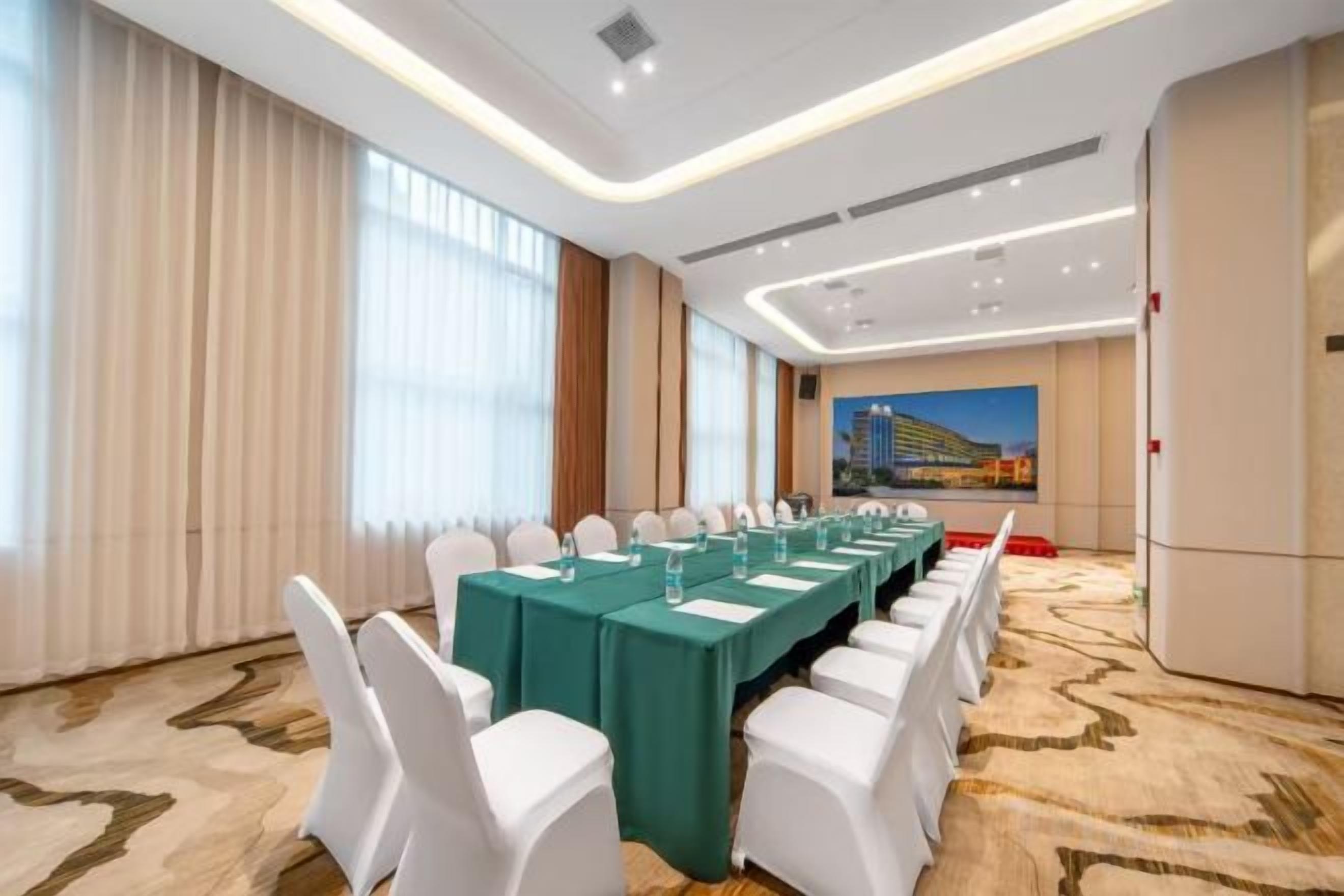 Un salón de conferencias con una mesa larga, sillas blancas y suelo alfombrado.
