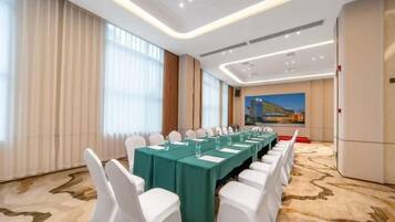 Un salón de conferencias con una mesa larga, sillas blancas y suelo alfombrado.