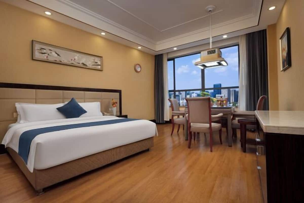 Habitación de hotel con una cama grande, un comedor y vistas a la ciudad a través del ventanal.