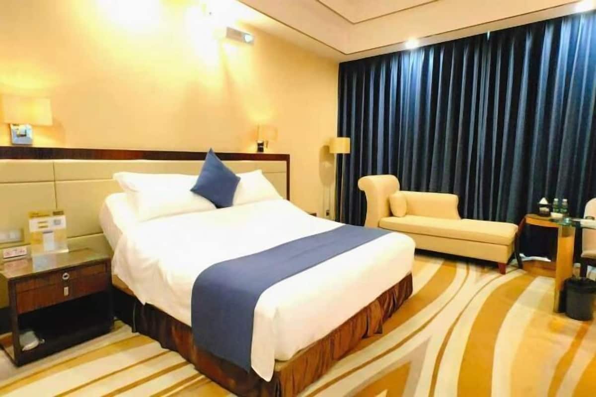 Una habitación de hotel con una cama grande, un sofá, una mesita de noche y una lámpara.
