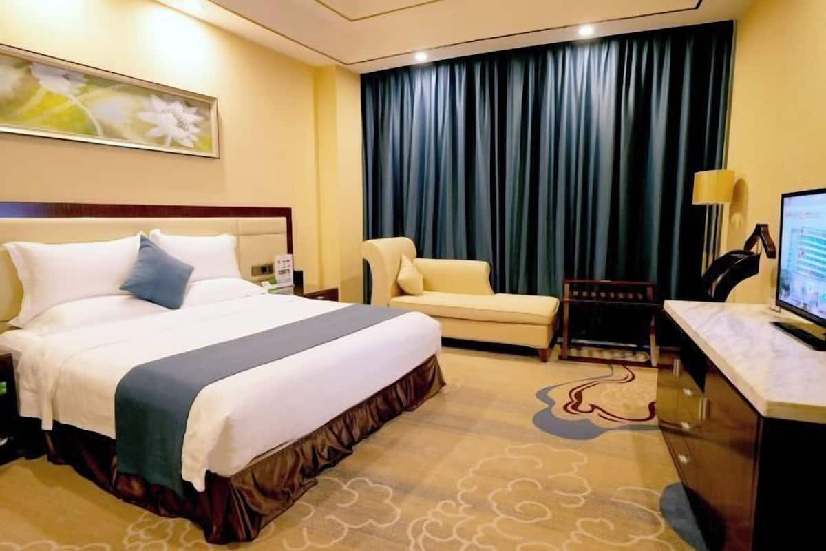 Habitación de hotel con cama, escritorio, silla, televisión y un ventanal con cortinas.
