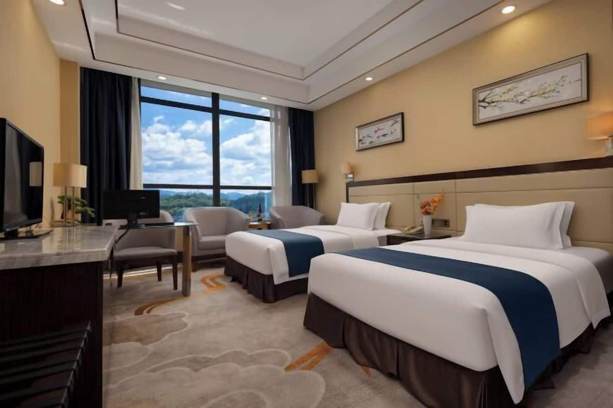 Habitación de hotel con dos camas, un escritorio, televisión y un amplio ventanal con vistas panorámicas.