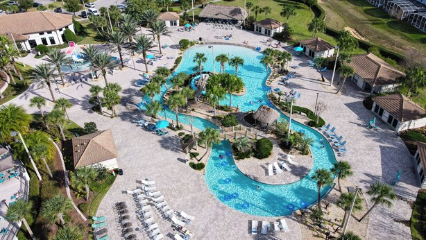Una vista aerea di un resort con una grande piscina sinuosa, lettini e palme.