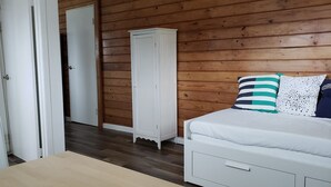 A bedroom with a wooden floor, a white wardrobe, a bed with striped pillows, and a white door. - Studio across the street from beach (Hauula)