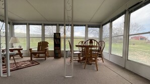 A covered patio area with a table and chairs, a bookshelf, and a lamp. - Life at the Dairy Farm (New Enterprise)