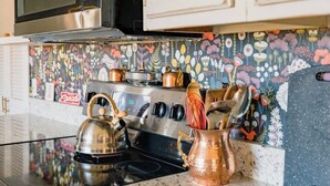 Une cuisine équipée d’une cuisinière en acier inoxydable, d’une bouilloire et de casseroles en cuivre posées sur le plan de travail.