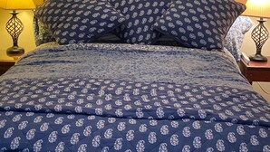 A neatly made bed with a blue floral bedspread and matching pillows, flanked by two wall-mounted lamps. - Spacious country home in a peaceful setting. New listing with frequent updates! (Red Wing)