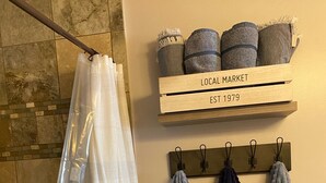 A bathroom with a shower curtain, towels, and a shelf labeled 'LOCAL MARKET EST 1979'. - Spacious country home in a peaceful setting. New listing with frequent updates! (Red Wing)