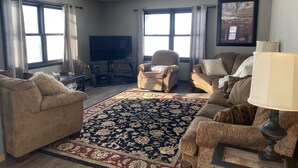 A living room with a large flat-screen TV, two armchairs, a sofa, a patterned rug, and a lamp. - Spacious country home in a peaceful setting. New listing with frequent updates! (Red Wing)