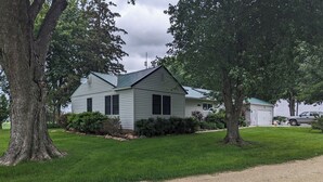 A single-story house with a sloped roof, surrounded by a well-maintained lawn and large trees. - Spacious country home in a peaceful setting. New listing with frequent updates! (Red Wing)
