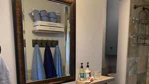 A bathroom with a large mirror, a sink, a shower, and a storage cart.