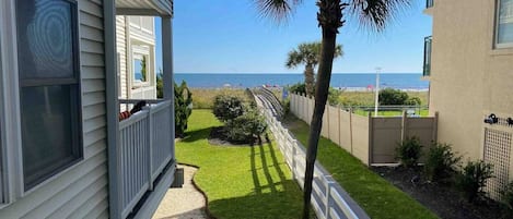 A coastal property with a balcony overlooking the beach, a well-maintained lawn, and a palm tree.