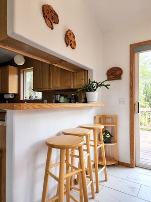A kitchen with wooden cabinets, a white countertop, and a potted plant. There are three wooden stools and a wooden chair.