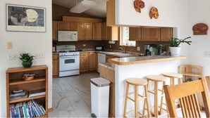 A kitchen with wooden cabinets, a microwave, a stove, a sink, and a small dining area with stools. - Alaska Fly In / Drive In, Kenai Peninsula Lodging (Sterling)