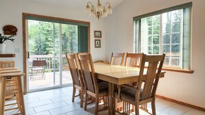 A dining room with a wooden table and chairs, large windows, and a chandelier. - Alaska Fly In / Drive In, Kenai Peninsula Lodging (Sterling)
