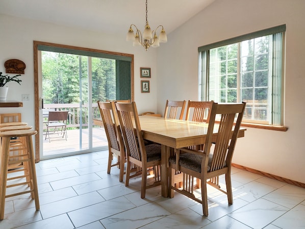A dining room with a wooden table and chairs, large windows, and a chandelier.
