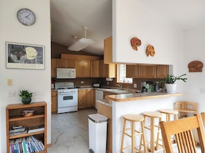 A kitchen with wooden cabinets, a microwave, a stove, a sink, and a small dining area with stools.