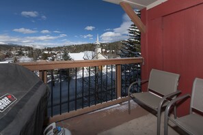 Enjoy a serene view of the snow-covered landscape from this balcony, featuring a barbecue grill and comfortable seating for two.