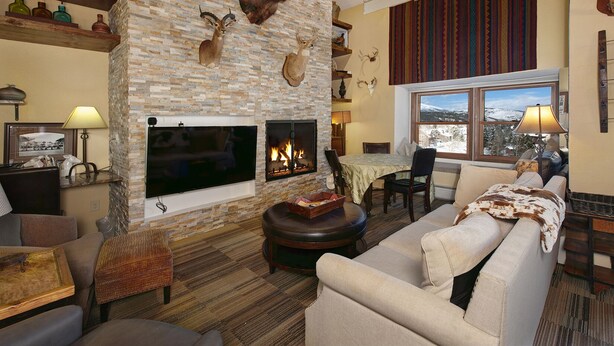 A cozy living room with a stone fireplace, a television, and a dining area with a view of the mountains. - Downtown Location walk to Main Street and Gondola from this updated Condo (Breckenridge)
