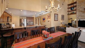 A spacious kitchen with a central island, wooden dining table with chairs, and a living area with a sofa and TV. - Downtown Location walk to Main Street and Gondola from this updated Condo (Breckenridge)