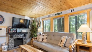 A cozy living room with a stone fireplace, a grey sofa, a wooden coffee table, and a television mounted on the wall.