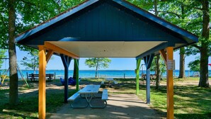 A covered picnic area with benches and a table, overlooking a beach.