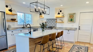 A modern kitchen with a central island, bar stools, pendant lighting, and a patterned backsplash.