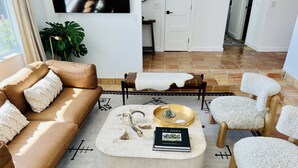 A living room with a brown sofa, a round coffee table with decorative items, a white furry chair, and a patterned rug.