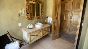 Un baño con tocador de madera, un espejo grande y una puerta que da a otra habitación.