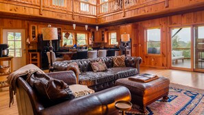 A spacious wooden cabin with a large living area featuring leather furniture, a kitchen, and large windows. - Jewel of the Woods - Magnificent Views from an Incredible Lodge! (Clayton)