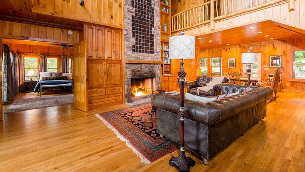 A spacious living room with a fireplace, leather sofa, and wooden floors. - Jewel of the Woods - Magnificent Views from an Incredible Lodge! (Clayton)
