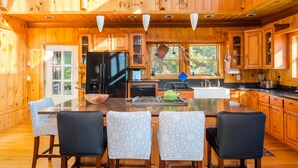 A wooden cabin with a large kitchen featuring a central island, dining table, and chairs. - Jewel of the Woods - Magnificent Views from an Incredible Lodge! (Clayton)